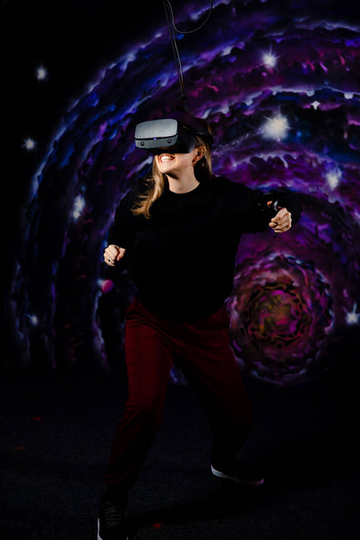 Ein junges Mädchen spielt mit einer VR-Virtual-Reality-Brille in einem Videospiel Schlachten. Raumhintergrund, Sterne und Planeten.  - Foto, Bild