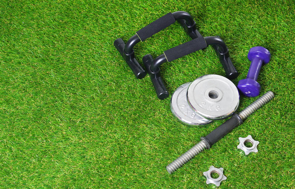 Fitness tools for physical training on the green artificial grass. Push up bars, dumbbells on the artificial turf. Copy space. - Photo, image