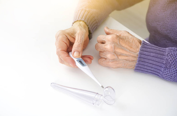 Body temperature measurement in elderly concept. An elderly woman hands at a thermometer. - Fotó, kép