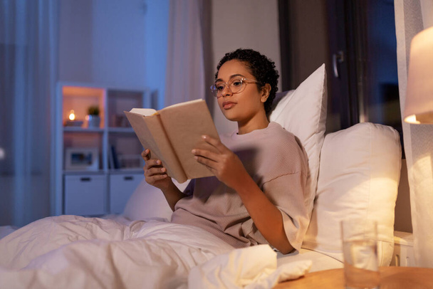 young woman in glasses reading book in bed at home - Foto, afbeelding