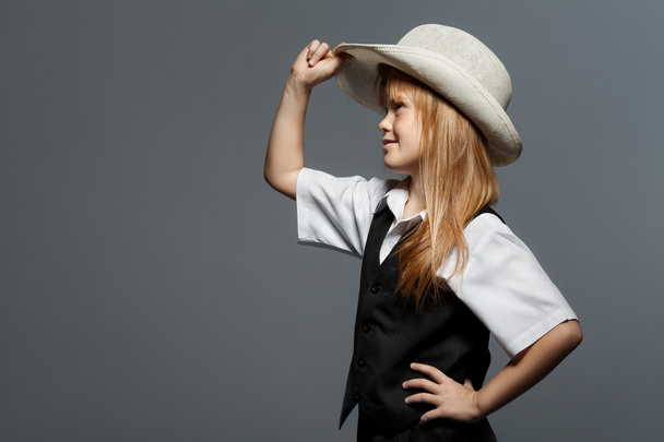 Pieni söpö tyttö hattu, valkoinen paita, musta liivi, etsii sivuun. eristetty harmaalla pohjalla
 - Valokuva, kuva