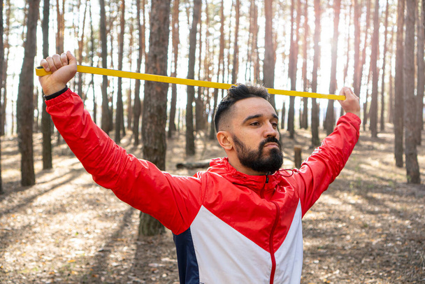 Free man excited with arms up pulling the resistance band in a forest. Enjoying the moment of being in nature. Healthy lifestyle background. - Φωτογραφία, εικόνα