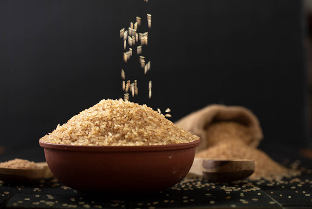 Kerala Matta rice _ parboiled rice or palakadan matta or red rice arranged in a earthenware and grains falling, with burlap saack of rice behind it, kitchen background., selective focus. - Foto, Imagem