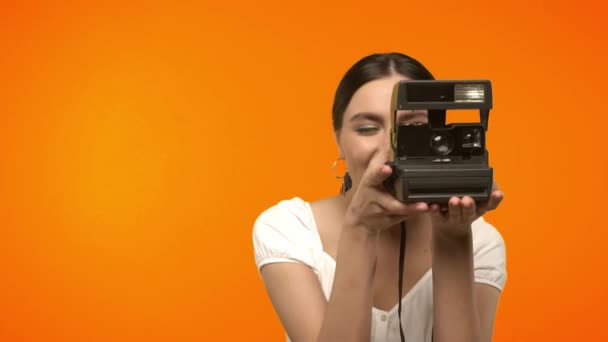 donna sorridente utilizzando fotocamera vintage isolato su arancione  - Filmati, video
