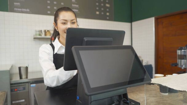 Азійська жінка бариста працює в фартусі на машині системи POS з чистим монітором порожніх екранів на стійці, кафе ресторану. офіціантка в кав'ярні. Життя людей. Бізнес обслуговування - Фото, зображення
