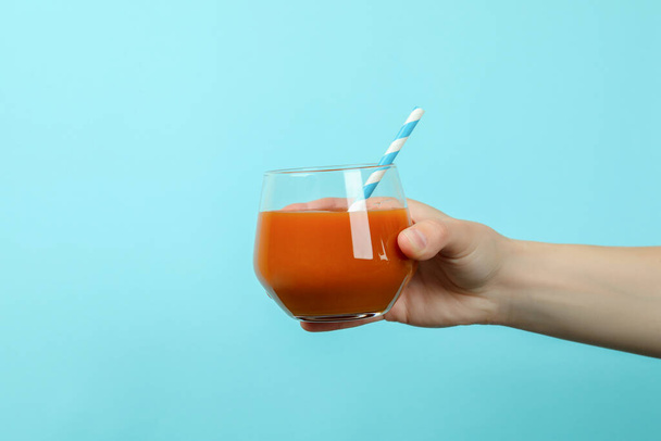 Female hand hold glass of juice on blue background - 写真・画像