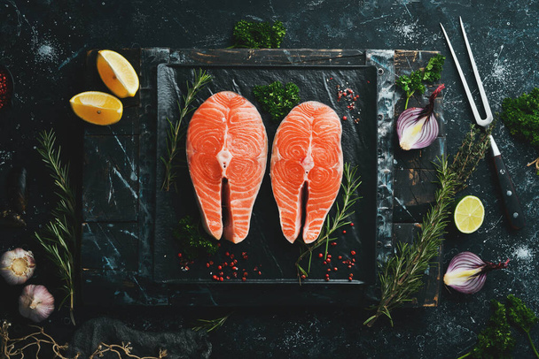 Two raw salmon steak with rosemary on a black stone plate. On a dark background. Top view. - Foto, imagen