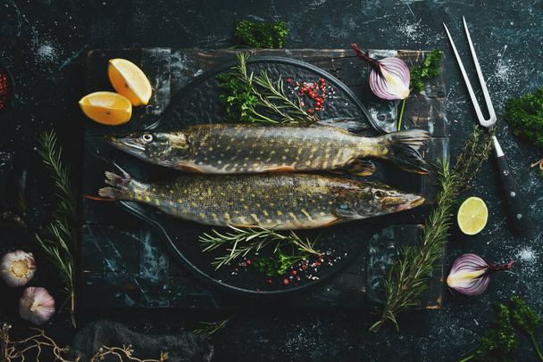 Two fish Pike with spices on a black stone plate. On a dark background. Top view. - 写真・画像
