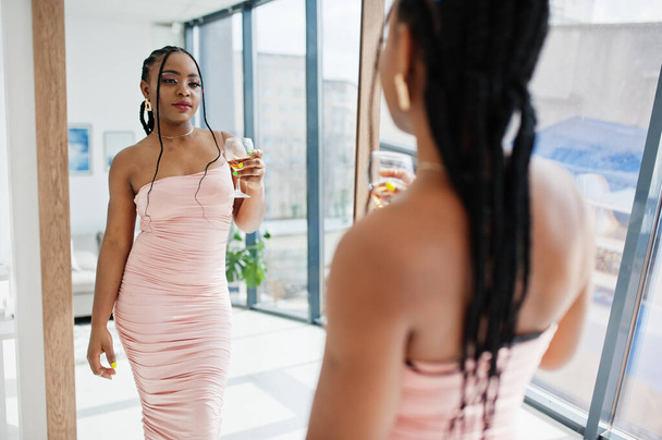 Fashionable photo of young beautiful romantic african american woman with glass of wine, wearing pink dress look at mirror. Summer, spring style. - 写真・画像