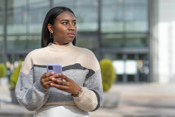 νεαρή μαύρη γυναίκα που χρησιμοποιεί το smartphone της στην πόρτα ενός εμπορικού κέντρου - Φωτογραφία, εικόνα