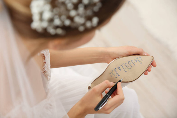 Young bride writing her single friends names on shoe indoors, closeup. Wedding superstition - Fotoğraf, Görsel