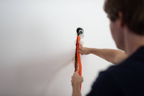 Přes rameno pohled na mladého muže umístění oranžové vlnité elektrické trubice do stěny v diy konceptuální obraz. - Fotografie, Obrázek