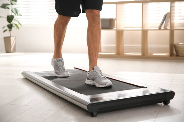 Sporty man training on walking treadmill at home, closeup - Fotó, kép