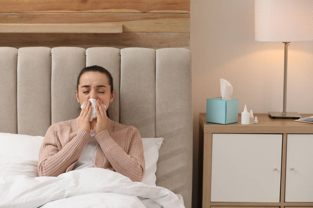 Sick young woman with napkins and nasal spray in bed at home - Fotografie, Obrázek