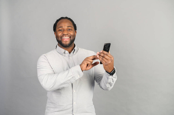 Hymyilevä Afrikkalainen Amerikan kanssa älypuhelin mies eristetty harmaa - Valokuva, kuva