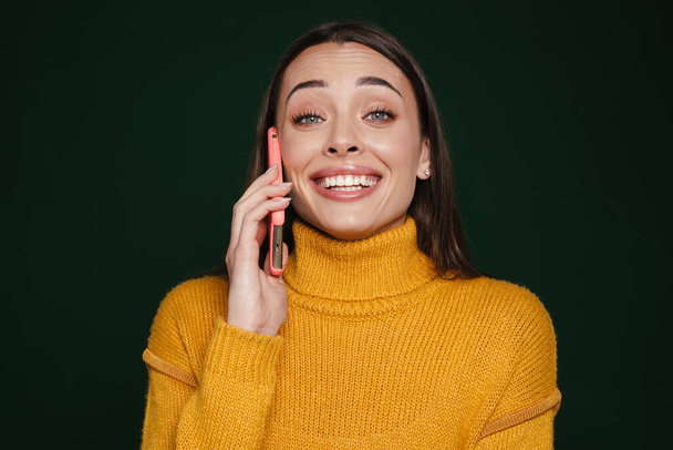 Freudiges schönes Mädchen lächelt und telefoniert isoliert auf grünem Hintergrund - Foto, Bild