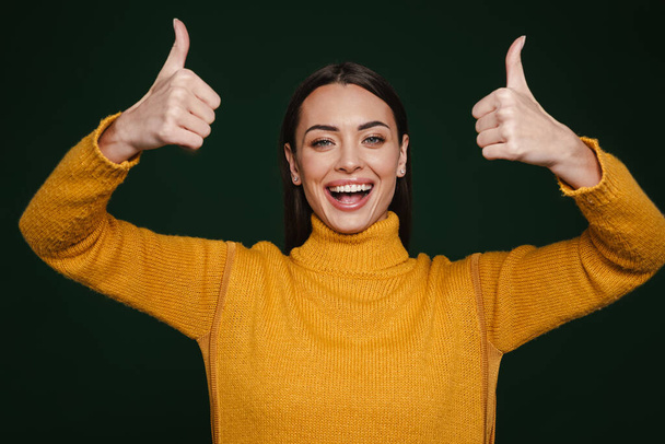 Joyful beautiful girl laughing and showing thumbs up isolated over green background - Foto, Imagem