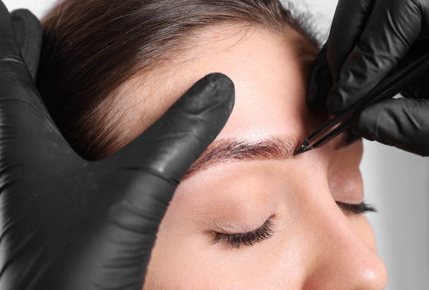 Beautician tweezing woman's eyebrow on light background, closeup - Foto, immagini