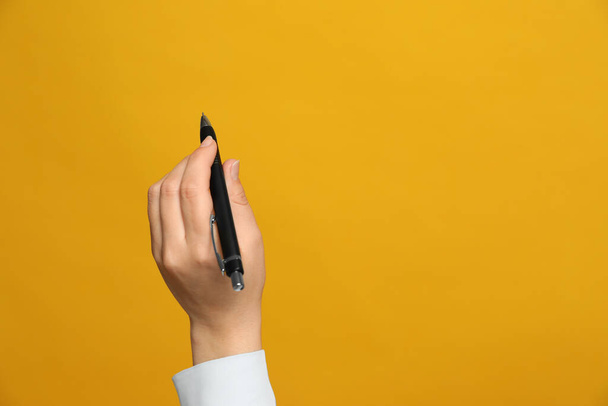 Left-handed woman holding pen on yellow background, closeup. Space for text - Фото, изображение