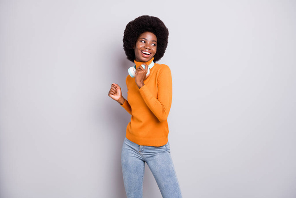 Photo portrait of afro american woman looking to side dancing holding earphones isolated on clear grey colored background - Foto, immagini