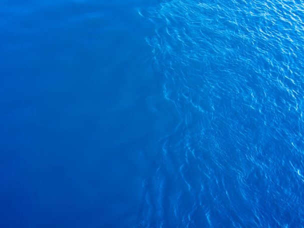 Widok z góry na jasnoniebieską wodę. Jedna część jest spokojna, druga część powierzchni pokryta jest falami. Streszczenie naturalnego tła z teksturą wody. - Zdjęcie, obraz