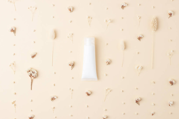 Tubo blanco de crema cosmética con flores sobre fondo beige pastel. Puesta plana - Foto, imagen