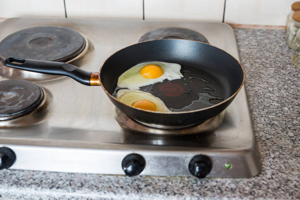 Eggs frying on stove top pan. Group of sunny side up eggs with yellow yolks cooking in silver skillet. - Photo, Image