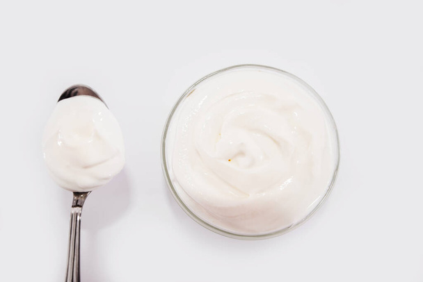 Teller und Löffel gefüllt mit saurer Sahne, Joghurt oder Soße auf weißem Hintergrund. Blick von oben. - Foto, Bild