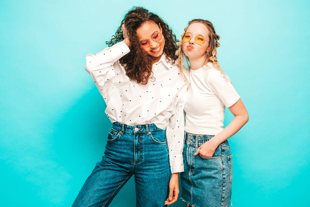 Dvě mladé krásné usměvavé mezinárodní hipsterky v módních letních šatech. Sexy bezstarostné ženy pózující u modré zdi ve studiu. Pozitivní modely se baví. Pojem přátelství - Fotografie, Obrázek