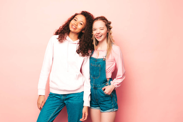 Two young beautiful smiling international hipster female in trendy summer clothes. Sexy carefree women posing near pink wall in studio. Positive models having fun. Concept of friendship  - Фото, зображення