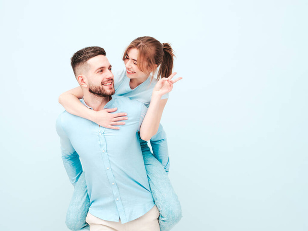 Smiling beautiful woman and her handsome boyfriend.Happy cheerful family having tender moments near light blue wall in studio.Pure models hugging.Embracing each other.Male gives piggyback riding - Photo, Image