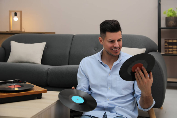 Happy man choosing vinyl record to play with turntable at home - Fotó, kép