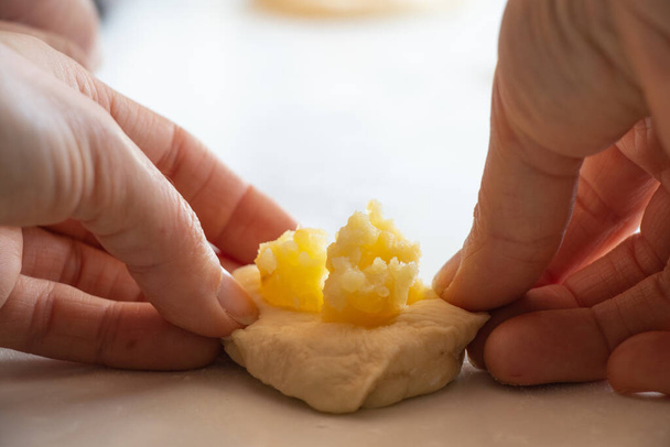 der Prozess der Zubereitung von Kuchen mit Kartoffeln zu Hause in der Küche auf einem weißen Tisch, hausgemachte Gewohnheiten mit Kartoffeln - Foto, Bild