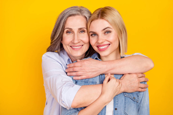 Photo portrait of mother and daughter smiling hugging holding hands isolated vivid yellow color background - Фото, зображення