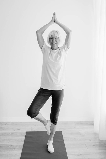 Monochromatyczny portret starszej kobiety uprawiającej jogę w domu. Anti wiek, sport, koncepcja jogi - Zdjęcie, obraz