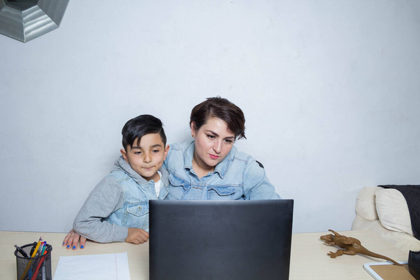 Η μαμά και ο γιος παρακολουθούν online μαθήματα στην οθόνη του φορητού υπολογιστή. Μεξικανική οικογένεια - Φωτογραφία, εικόνα