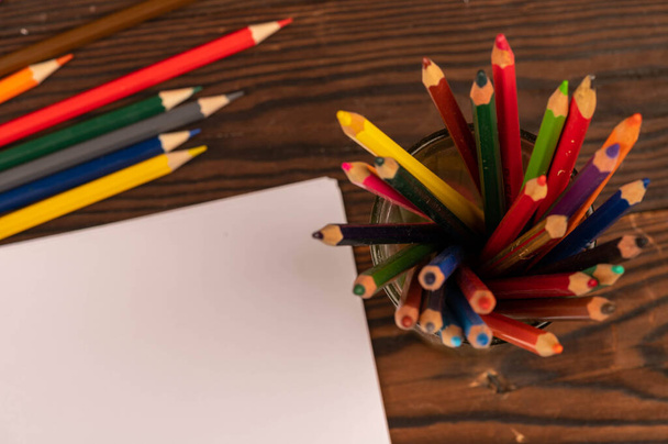 Színes ceruzák és fehér papírlapok egy fa asztalon. Közelkép szelektív fókusz. - Fotó, kép
