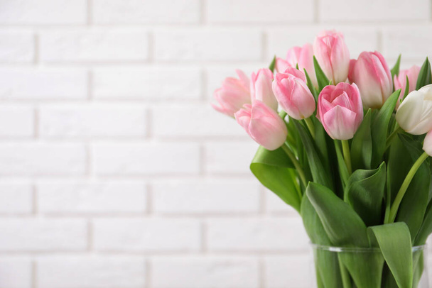 Beautiful bouquet of tulips in glass vase against white brick wall. Space for text - Fotoğraf, Görsel
