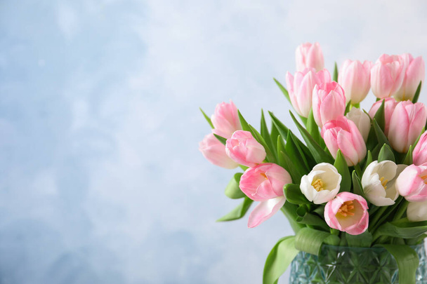 Beautiful bouquet of tulips in glass vase against light background. Space for text - Fotoğraf, Görsel