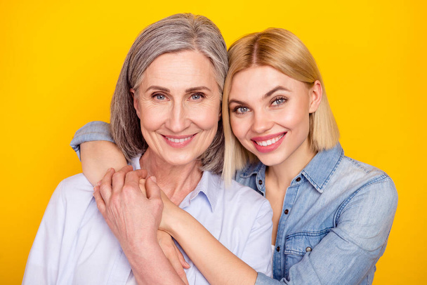Photo portrait of mother and daughter embracing together smiling holding hands isolated vivid yellow color background - Foto, Imagen
