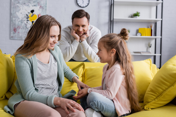 Smiling girl sitting near mother and blurred father in living room  - Fotoğraf, Görsel