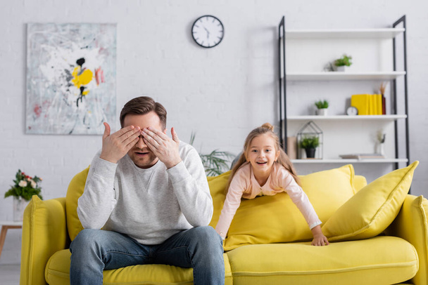 Pai cobrindo olhos perto de criança alegre na sala de estar  - Foto, Imagem