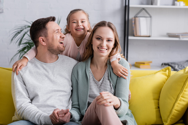 Kid embracing happy parents on sofa at home  - Foto, afbeelding