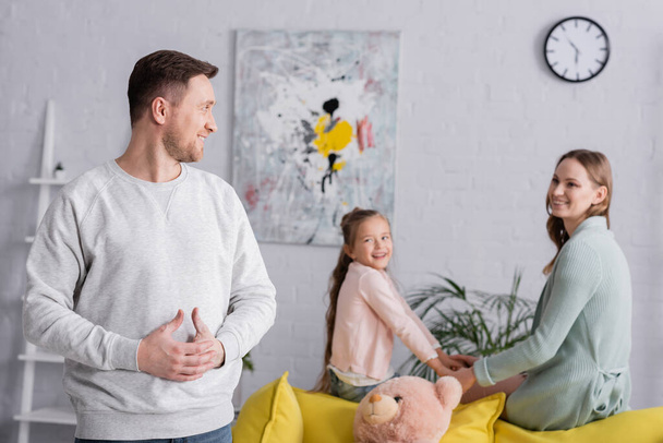 Smiling man looking at family on blurred background at home  - Foto, Bild