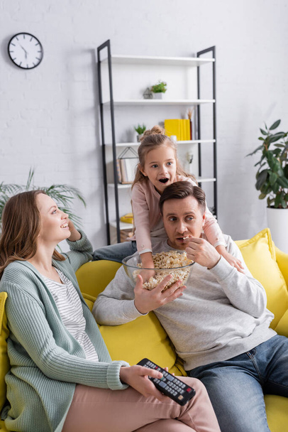 Man holding popcorn near daughter and wife with remote controller  - Fotoğraf, Görsel