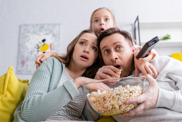 Scared family with popcorn watching film on couch  - 写真・画像