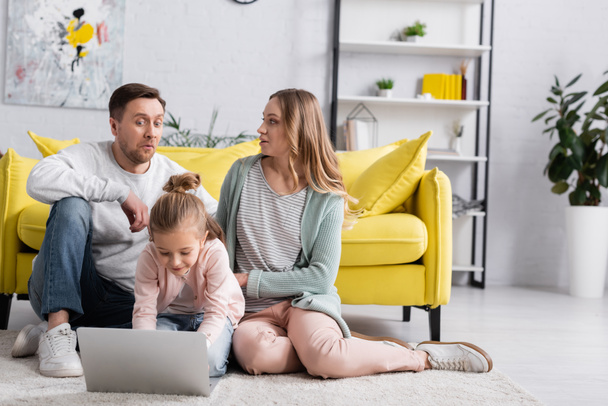 Child using laptop near excited parents on floor at home  - Photo, Image