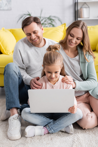Child using laptop near smiling parents on blurred background at home  - Valokuva, kuva