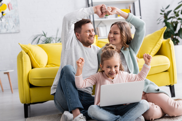 Vidám lány laptoppal mutatja igen gesztus közelében szülők a nappaliban  - Fotó, kép