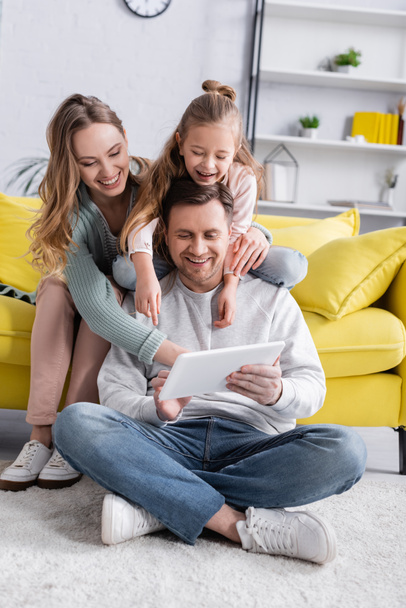 Man using digital tablet on floor near family on couch  - Fotó, kép